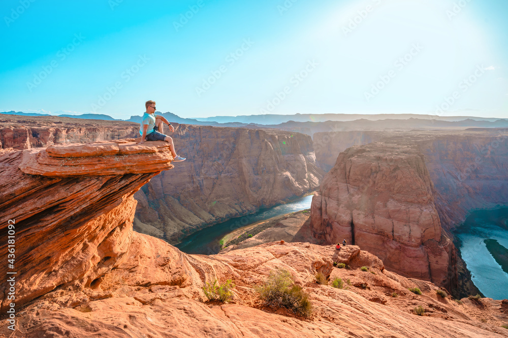 Wall mural A young man stands on top of a cliff facing a horseshoe bend in the town of Page. Amazing scenery in Arizona.