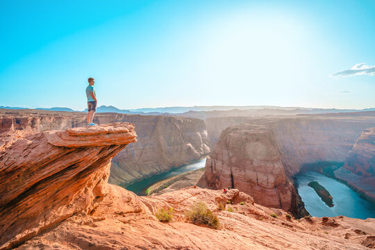 A young man stands on top of a cliff facing a horseshoe bend in the town of Page. Amazing scenery in Arizona.