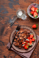 Fototapeta na wymiar Mini chocolate pancake cereal with strawberries for breakfast on old wooden table. Trendy home breakfast with tiny pancakes. Top view