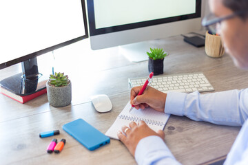 Latino man working in front of the computer taking notes in his agenda
