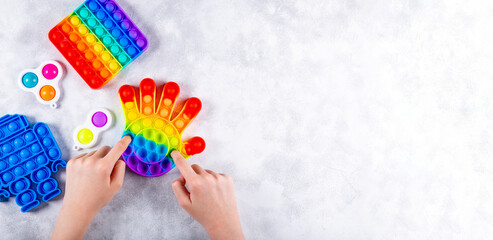 Banner for web site with copy space for text. Children hands are playing a new trendy silicone toy antistress pop it, next to other toys pop it and simple dimple. Top view