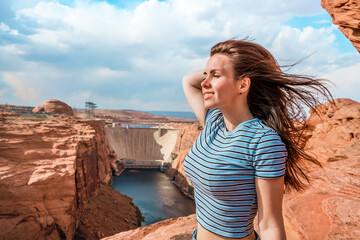 A young woman on red rocks admires the view of Glen Canyon Dam, Arizona