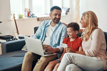 Young beautiful family shopping online and smiling while using laptop at home