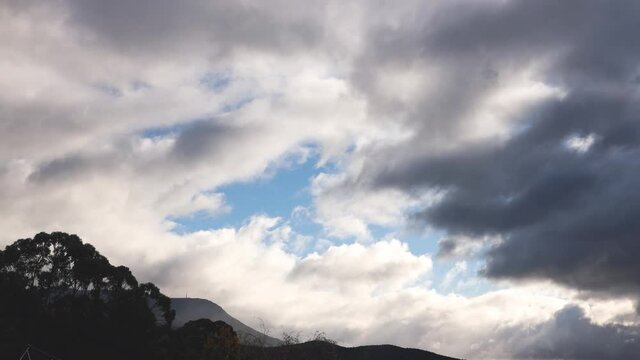 timelapse of cloud rolling over the mountains with sun rays peaking through shining over the thick vegetation, shot in Tasmania Australia in winter