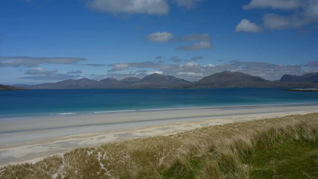 4k time lapse Luskentyre beach, Isle of Harris, on a sunny day. Cloud and light movement, unidentifiable people walking on beach. View over white sand and turquoise sea with mountains in background. 