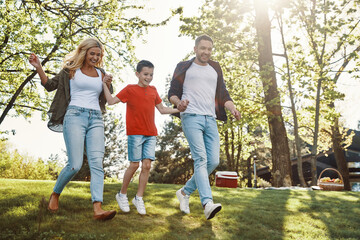 Happy young mother and father with little boy holding hands and walking outdoors