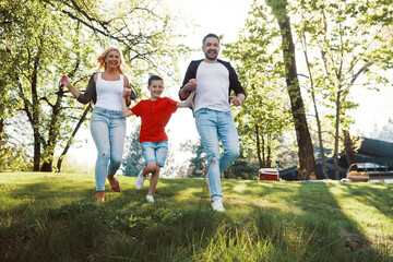 Happy young mother and father with little boy holding hands and walking outdoors
