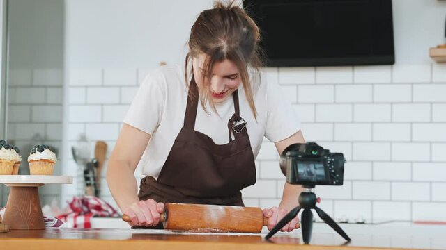 A woman pastry chef rolling out dough with rolling pin on the table and filming it on the phone camera