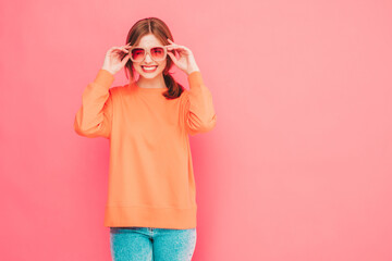 Young beautiful smiling female in trendy summer clothes. Sexy carefree woman posing near pink wall in studio. Positive model having fun in sunglasses. Cheerful and happy