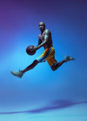 Fototapeta na wymiar Sportive athletic african-american male basketball player training in neon light on blue background.