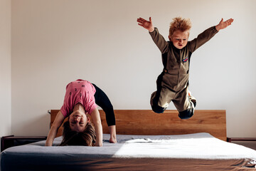 siblings playing in their parent's bedroom. kid aviator flying on the bed. girl athlete doing the...