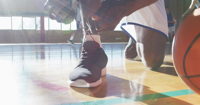African american male basketball player tying shoes with team in background
