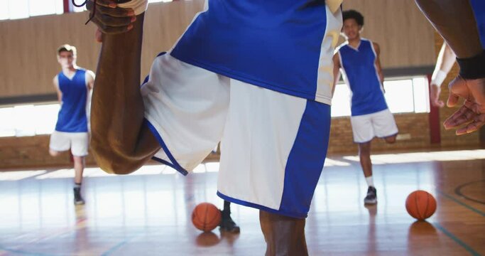 Diverse male basketball team wearing blue sportswear and stretching
