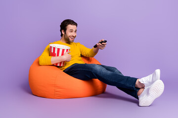 Full length body size photo guy in beanbag laughing watching tv keeping remote controller isolated pastel purple color background