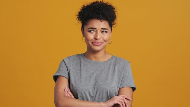 A beautiful american woman wearing gray basic T-shirt is listening the viewer and giving yes-no answers isolated over yellow wall in the studio