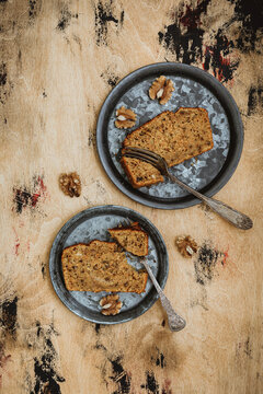 A vertical top view image of a carrot apple walnut loaf cake. Slices of cake on vintage metal plates, wooden backdrop.