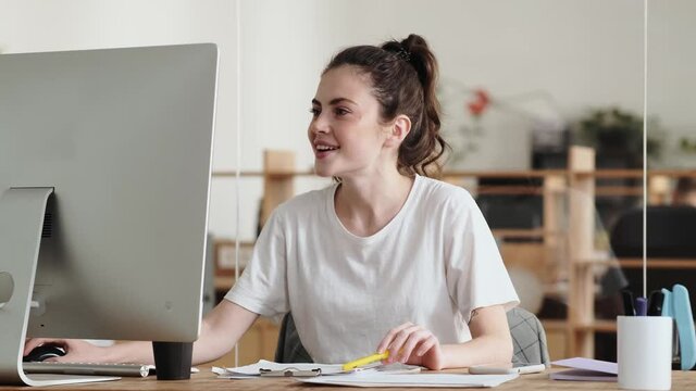 The pleasantly surprised woman looking into the monitor and typing something on the keyboard while sitting in the office
