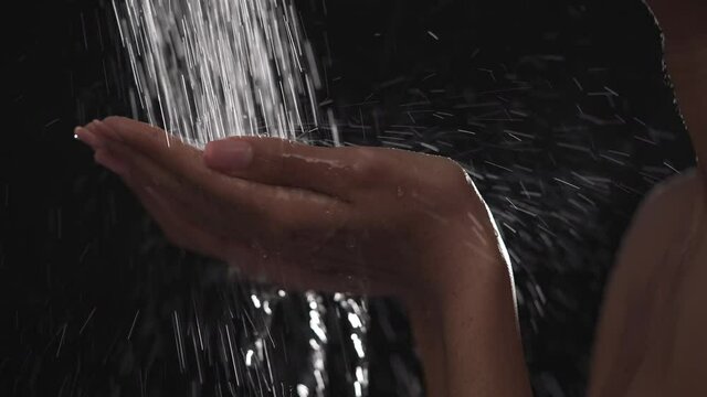 Close up of woman holding palms under running water. Female taking shower. Isolated on black background