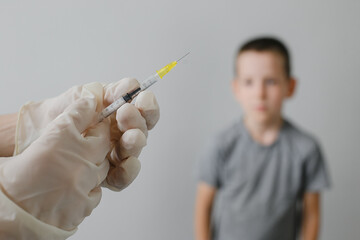 Doctor preparing vaccination injection with a syringe to an afraid child boy. Vaccination of children at school concept.
