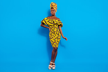 Full size photo of young beautiful lovely african woman in yellow dress and turban look copyspace isolated on blue color background