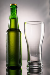 pouring beer into beer glass and foam and green transparent bottle with beer beside