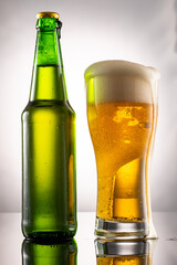 pouring beer into beer glass and foam and green transparent bottle with beer beside
