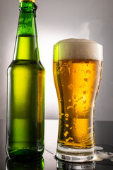 pouring beer into beer glass and foam and green transparent bottle with beer beside