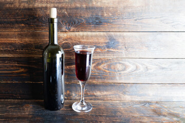 Wine bottle and wine glass on wooden plank surface.