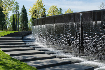 Fountain 'Infinity' in form of huge bowl. Waterfall flows in streams into granite bed of artificial...