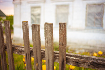 Old broken picket fence. White rural house in blurred background