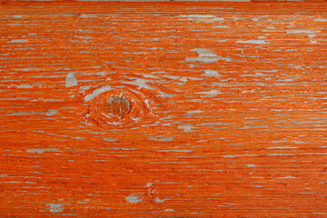 An old texture board with a knot, covered with peeling bright orange paint