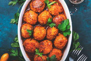 Meatballs with spicy tomato sauce in white baking dish on blue kitchen table. Top View