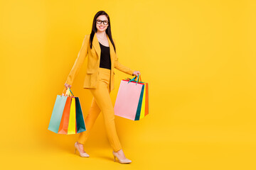 Full size photo of nice millennial young lady hold bags go wear eyewear yellow suit isolated on vivid color background