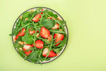 Strawberry Vegan Salad with spinach, arugula, walnuts, balsamic vinegar and olive oil dressing on lime green background. Healthy food. Top view
