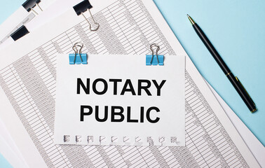 On a light blue background, documents, a pen and a sheet of paper on blue paper clips with the text NOTARY PUBLIC. Business concept.