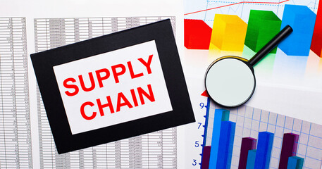Naklejka premium On the table there are reports of multi-colored charts, a magnifying glass and a sheet of paper in a black frame with the text SUPPLY CHAIN. Business concept