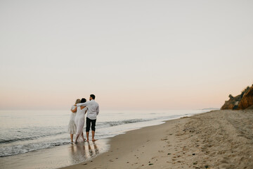 Back view of three adult humans hugging walking on the beach together. Concept of happiness.
