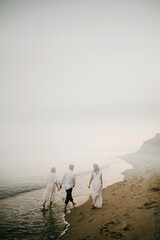 Three adult humans enjoying walking along the ocean. View from distance on two women and man on the beach.