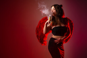 A girl smokes a VAPE on a red background. A young brunette with a VAPE in her hands in a cloud of smoke. Ads for e-cigarettes and accessories with space for text. A long-haired vaper girl.