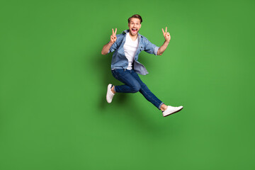 Fototapeta na wymiar Full length body size photo of young guy jumping happy showing v-sign gesture isolated vivid green color background