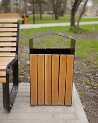 Cropped photo of wooden trash can and bench in the spring park against the background of trees.