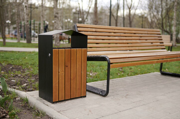 Wooden bench and trash can in the spring park against the background of trees.
