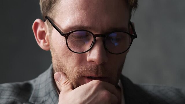 A close-up shot of a meditative man in an office suit and glasses looking forward and to the side in a gray office