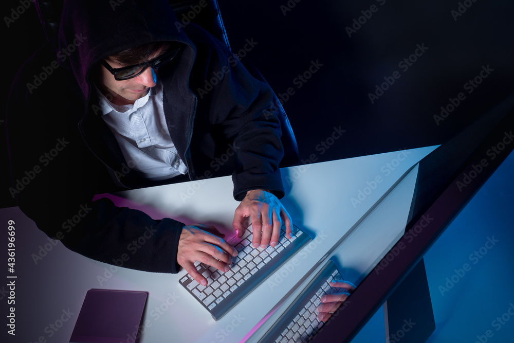 Poster a man in a black hoodie at the computer. the man at the computer is taken from above on a black back