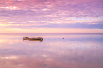 Lonely boat in the middle of the sea captured during sunset reflected in the water. Ebro Delta, Tarragona, Spain. - obrazy, fototapety, plakaty