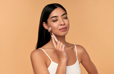 A young Asian woman with clean radiant skin makes a facial massage with a quartz roller on a beige...