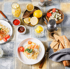 On the table is a plate of food, spaghetti with shrimp. Next to the baguette and glasses of water and lemon.