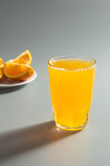 Orange carbonated drink in a glass and orange slices in a plate in the background.