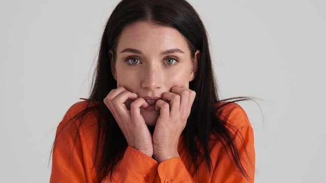A frightened woman is looking to the camera standing isolated over grey wall in the studio