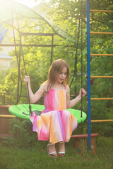 Cute girl in a beautiful summer dress swings on the swing